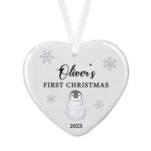 Heart-shaped ceramic Christmas decoration with a cute baby penguin illustration, personalised with the name Oliver, the phrase “First Christmas”, and the customisable year 2023. White hanging ribbon and snowflake details. Perfect personalised baby’s first Christmas tree ornament keepsake gift for new parents, grandparents, mum, dad, nana or family to celebrate a baby’s first festive season.