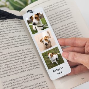 Personalised pet photo bookmark featuring three custom glossy images of a Jack Russell terrier with the customisable text 'Ralphie' on a white aluminium background. The bookmark is lying open in a book with a black tassel. Perfect gift for dog dads, cat mums, pet rabbit, guinea pig, or indoor bird owners for a birthday present idea.
