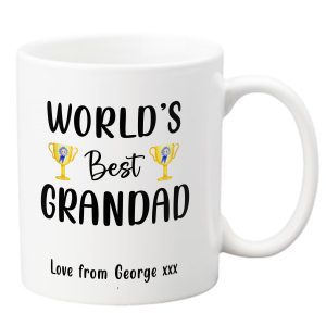 white ceramic mug with black text that reads world’s best grandad and features two gold trophy cup illustrations with blue rosettes plus a personalised message love from george xxx printed at the bottom, thoughtful personalised gift for grandad birthday father’s day or christmas present, custom coffee tea mug high quality dishwasher safe sentimental keepsake for grandad