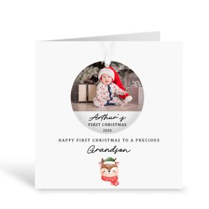 Personalised first Christmas grandson card with custom photo and removable acrylic bauble decoration, featuring a baby in a Santa hat sitting under a Christmas tree. Handmade keepsake card printed on luxury white 300gsm card with “Happy First Christmas to a Precious Grandson” text and cute festive reindeer illustration. Includes white ribbon for hanging ornament.